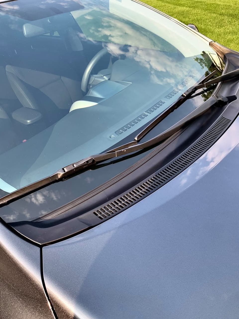 Clear windshield glass and a clean cowl panel with the wiper channel and vents free of debris